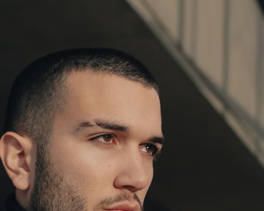 Side profile of a man with a buzz cut and trimmed beard on a plain studio background