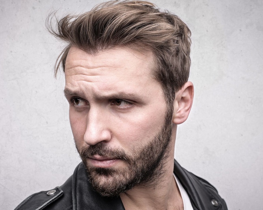 White British-looking man looking away with a classic textured short back and sides cut, visible length on the sides, and a neat short beard